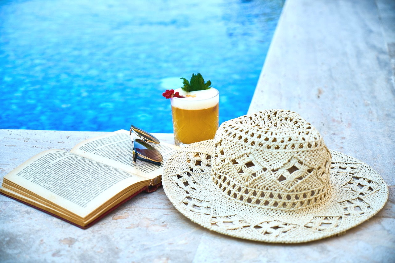 Symbolfoto Buch und Hut am Pool