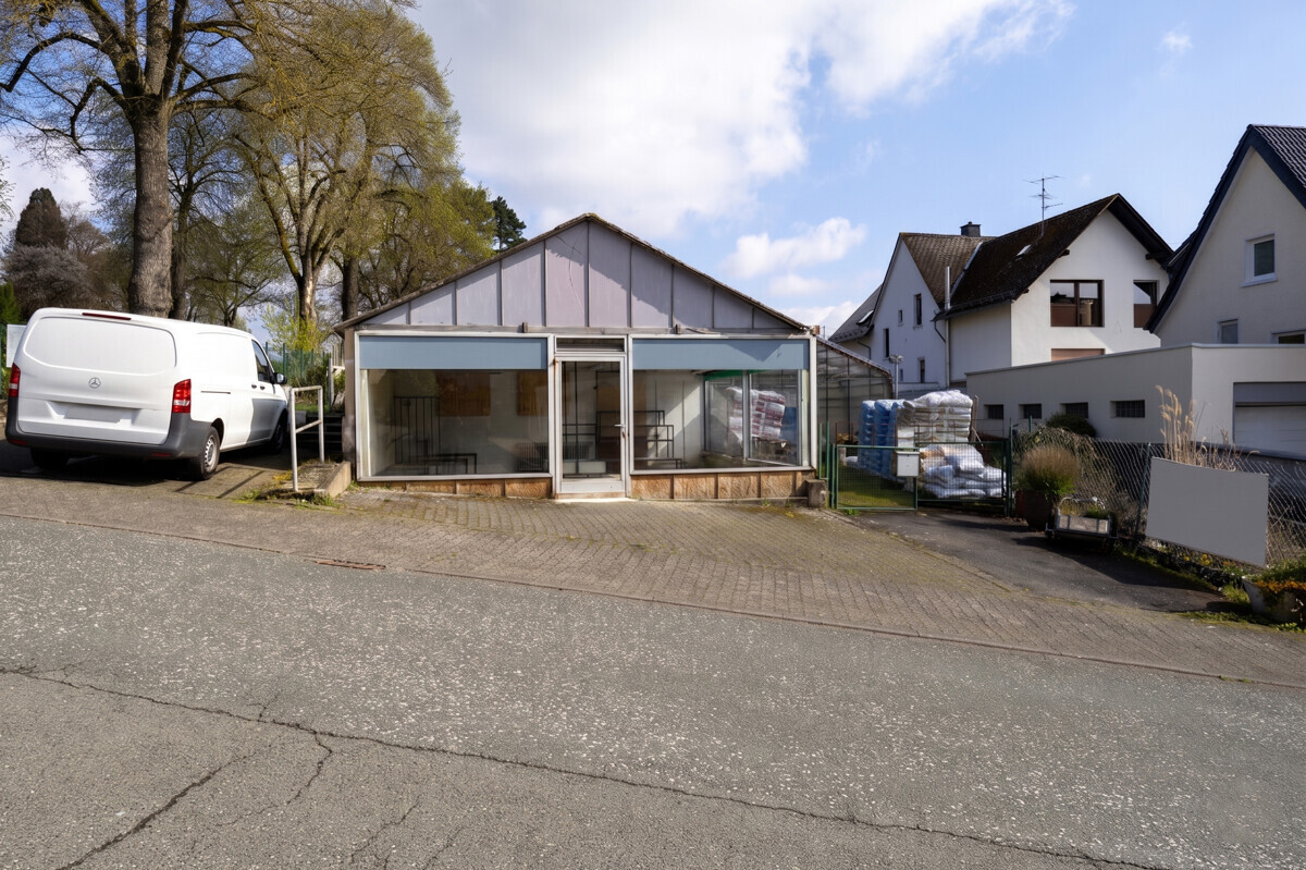 Straßenansicht des ehemaligen Verkaufsgebäudes der Gärtnerei mit großen Schaufenstern und Zufahrt auf dem Gewerbegrundstück in Siegen-Geisweid